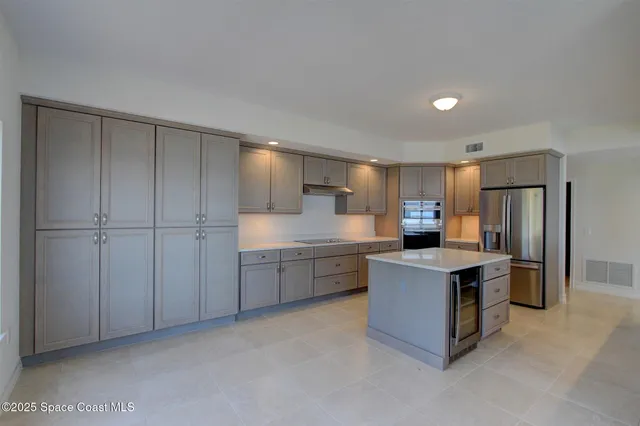 a large kitchen with stainless steel appliances a stove a sink a refrigerator and white cabinets with wooden floor