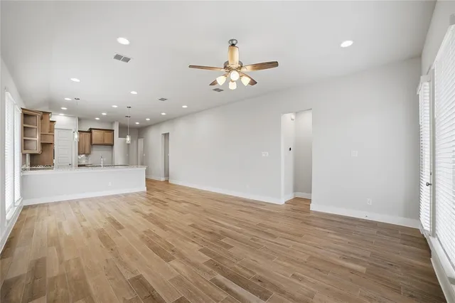 a view of an empty room and kitchen with wooden floor