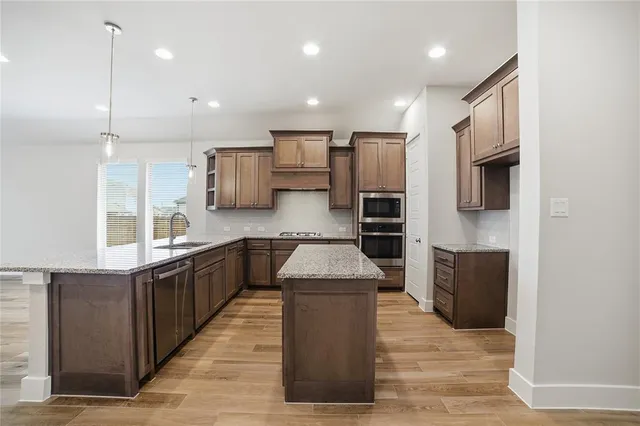 a large kitchen with stainless steel appliances kitchen island granite countertop a stove a refrigerator a sink dishwasher and wooden cabinets with wooden floor