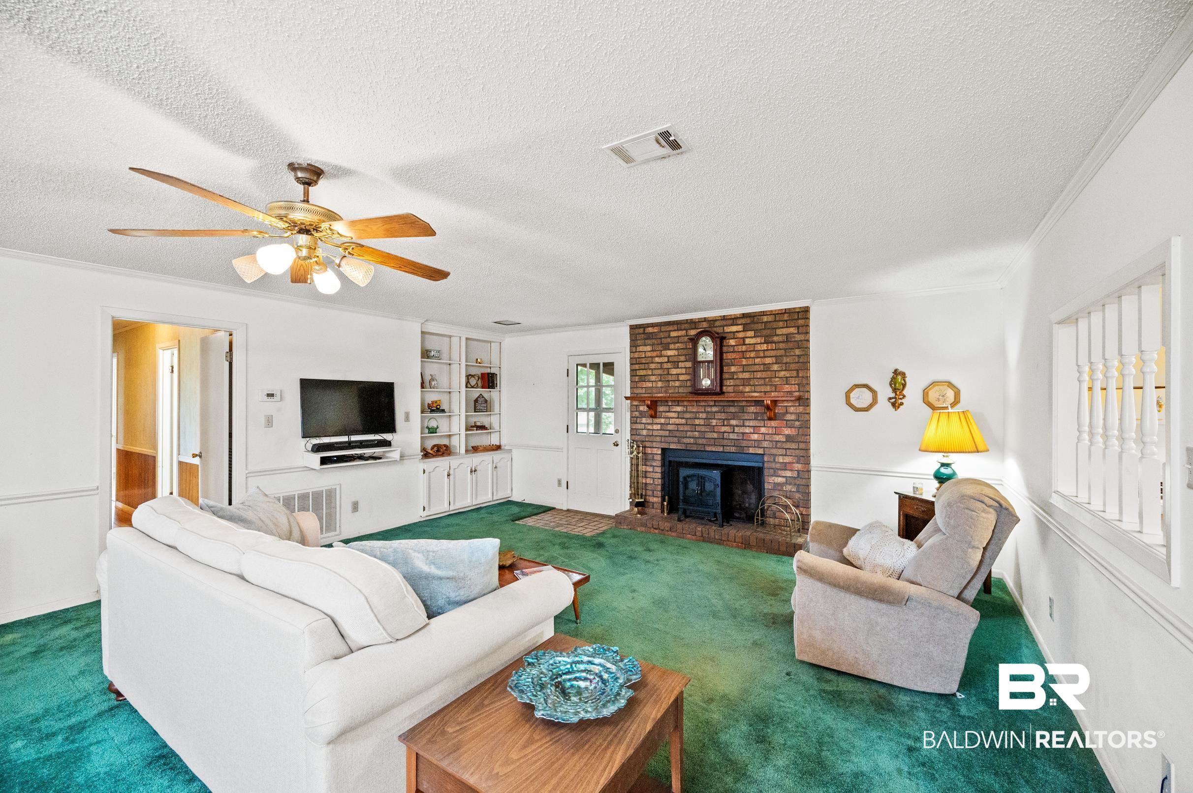 15600 Fackler Road Loxley, AL 36551 - Photo 3 of 51 Carpeted living room featuring a fireplace, a textured ceiling, ceiling fan, crown molding, and brick wall