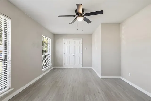an empty room with wooden floor fan and windows