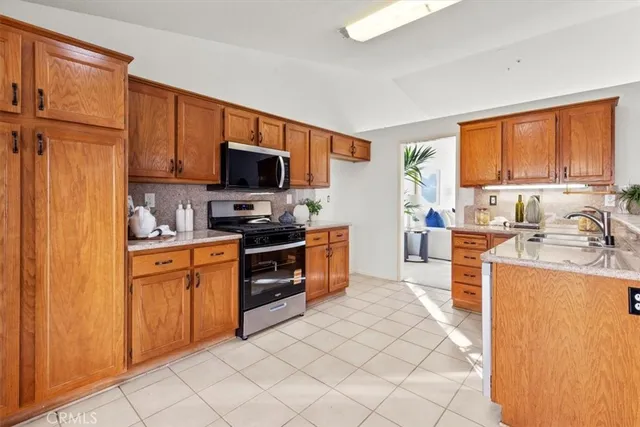 a kitchen with stainless steel appliances granite countertop a stove top oven a sink dishwasher and a refrigerator with wooden cabinets