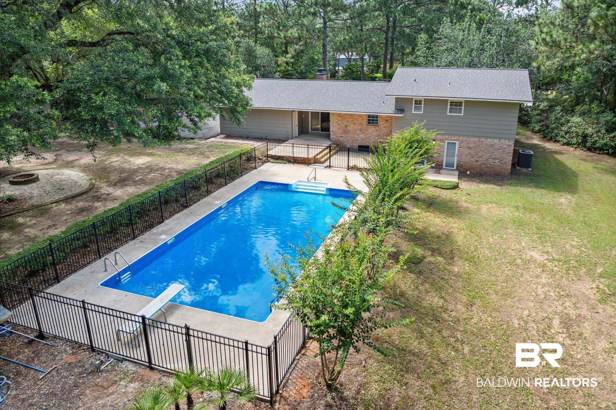 8301 Fordham Road Mobile, AL 36619 - Photo 52 of 57 Expansive backyard featuring a rectangular swimming pool with a diving board, surrounded by a concrete deck and black metal fencing