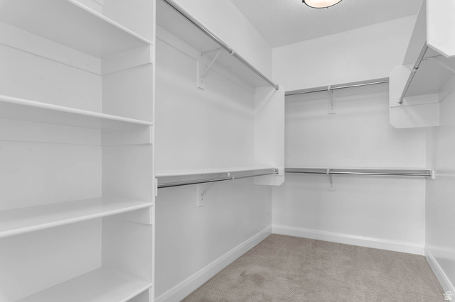 11673 South Halls Crk Road Draper, UT 84020 - Photo 22 of 22 Walk-in closet featuring built-in shelving, multiple hanging rods, white walls, white baseboards, and light-colored carpet flooring