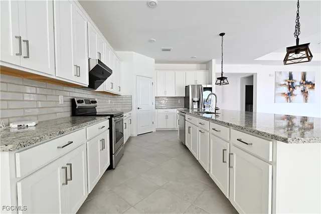 a kitchen with stainless steel appliances granite countertop white cabinets a sink a stove and a refrigerator