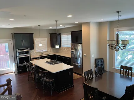 a kitchen with stainless steel appliances kitchen island granite countertop a dining table chairs and refrigerator