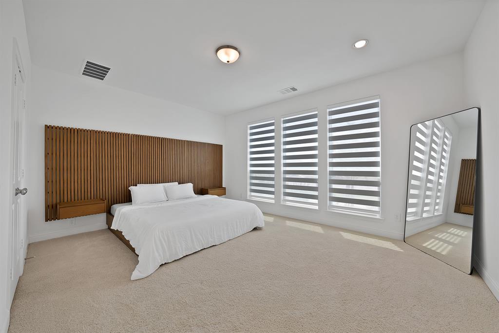 5012 Triadic Lane Prosper, TX 75078 - Photo 17 of 38 Expansive bedroom featuring a full-wall wood panel accent, three large windows with integrated blinds, and plush carpet flooring
