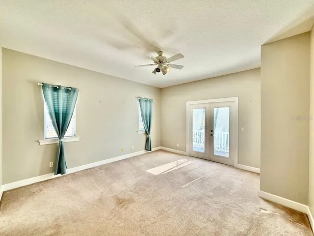 an empty room with chandelier fan and windows