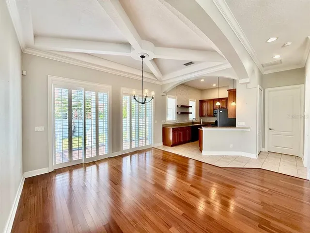 a view of an empty room with wooden floor and a kitchen