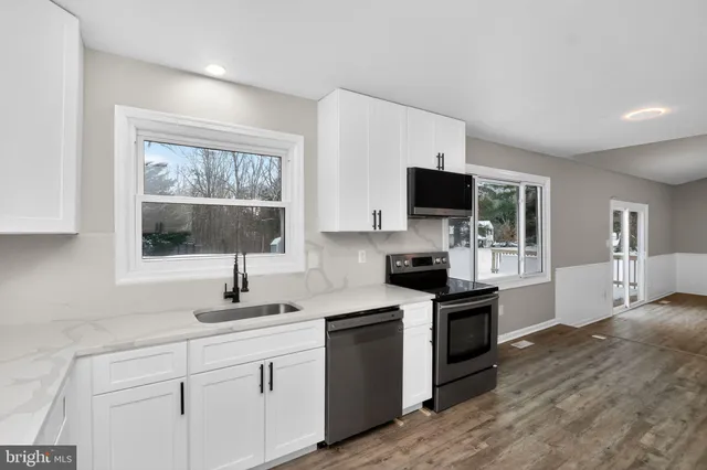 a kitchen with stainless steel appliances granite countertop a stove top oven a sink dishwasher and a microwave oven with white cabinets