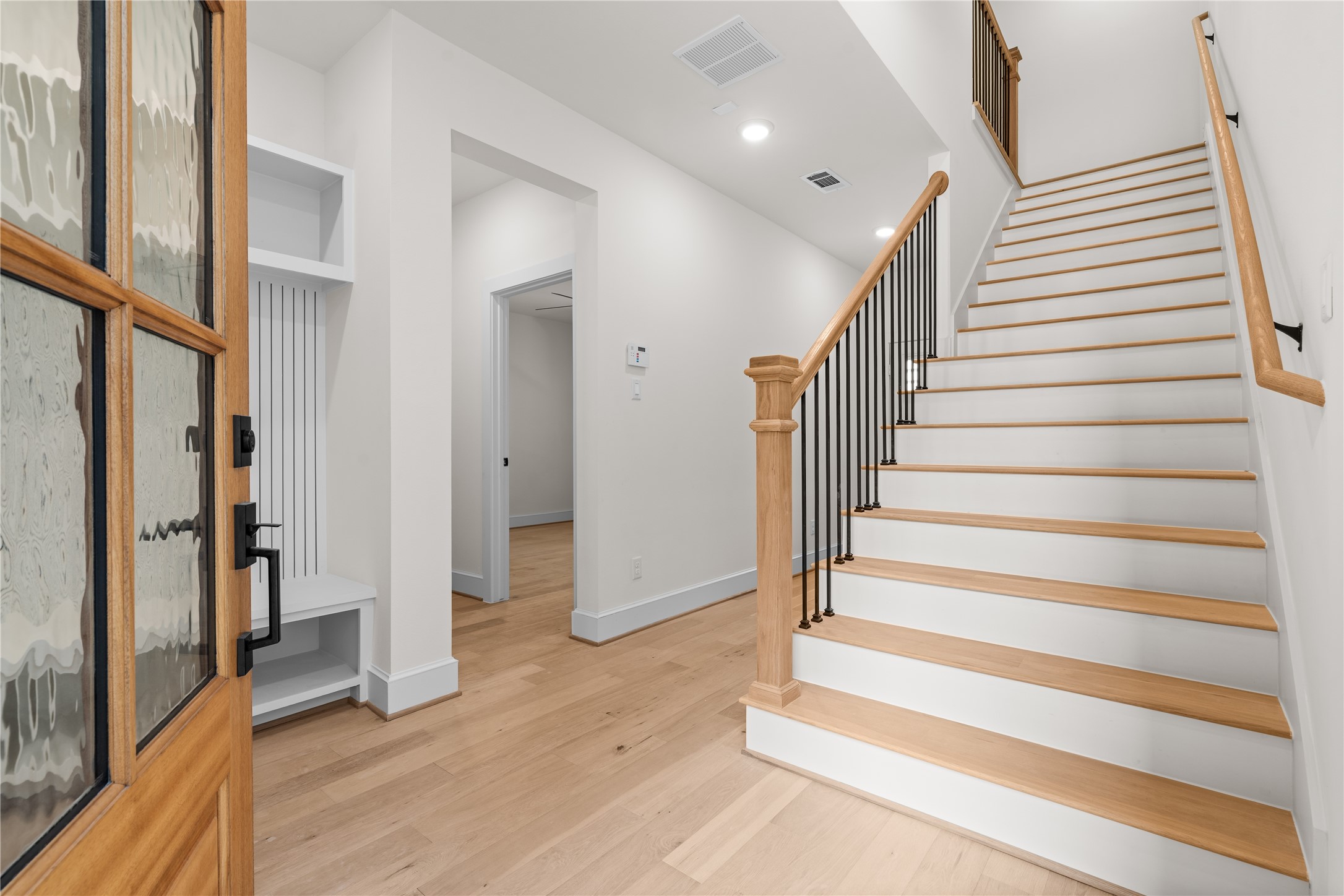 1614 Ojeman Road, Unit C Houston, TX 77055 - Photo 6 of 48 A bright entryway with a wooden front door, leading to a staircase with wooden steps and a metal railing. The space features white walls, engineered wood floors, and modern decor, creating a welcoming and contemporary atmosphere.