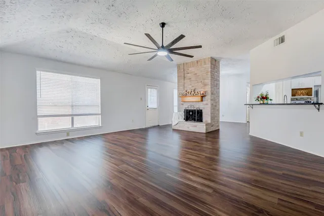 an empty room with wooden floor a ceiling fan a fireplace and windows