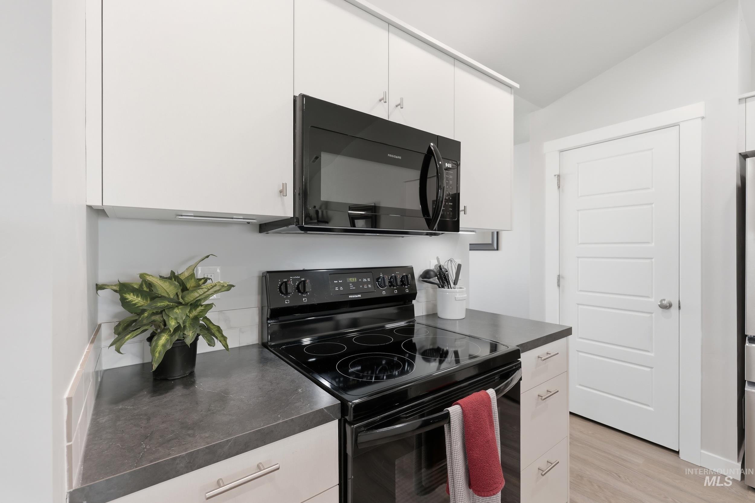 3697 W Lane Meridian, ID 83642 - Photo 13 of 44 Kitchen with black appliances, white cabinetry, dark countertops, LVP Flooring, and vaulted ceiling. Stainless Fridge