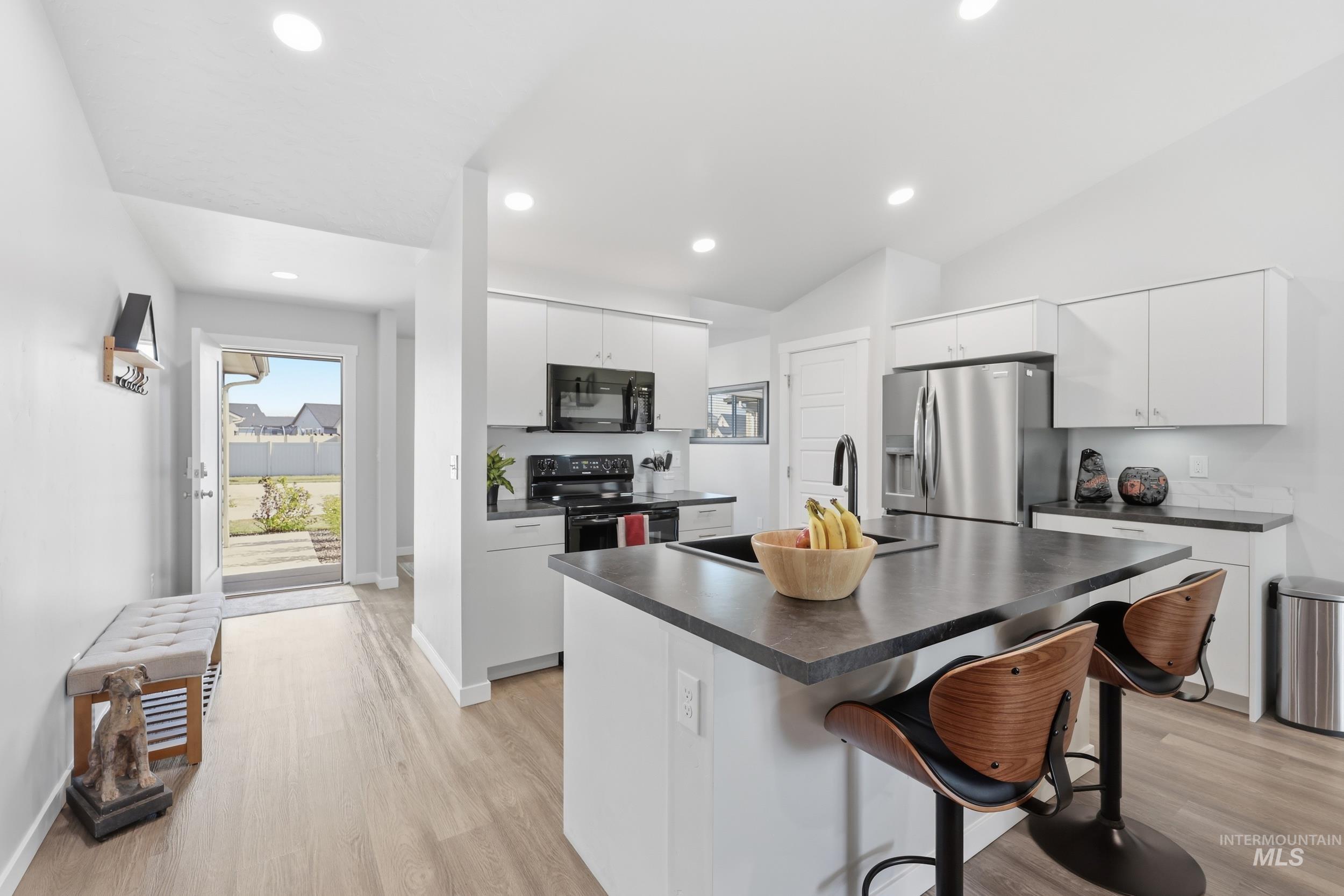3697 W Lane Meridian, ID 83642 - Photo 15 of 44 Kitchen featuring white cabinets, black appliances, stainless fridge a breakfast bar, a kitchen island with sink, and LVP Flooring