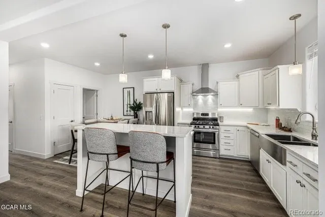 a kitchen with stainless steel appliances kitchen island granite countertop a stove top oven a sink dishwasher a refrigerator and white cabinets with wooden floor