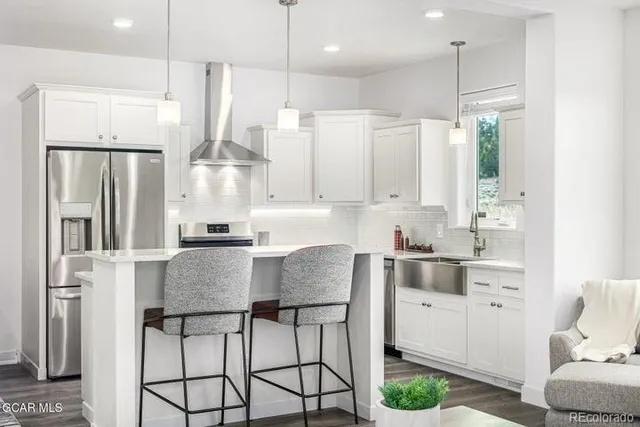 a kitchen with stainless steel appliances granite countertop a refrigerator a sink dishwasher a stove and white cabinets with wooden floor