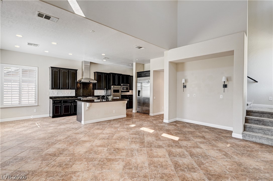 2793 Rosenhearty Drive Henderson, NV 89044 - Photo 12 of 85 An open concept living area showcasing a contemporary kitchen with dark cabinetry and a central island, flowing into a spacious tiled floor.