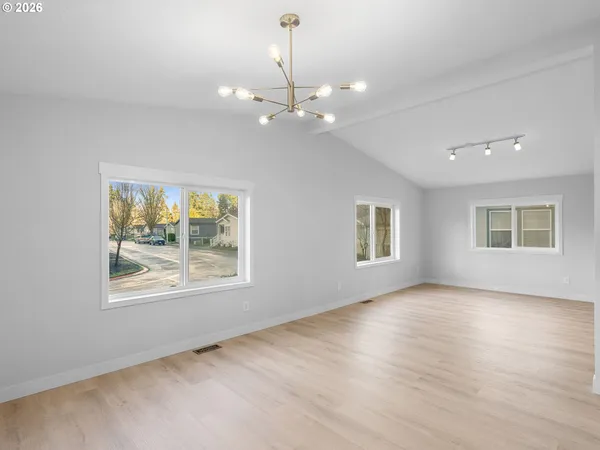 an empty room with wooden floor chandelier and windows