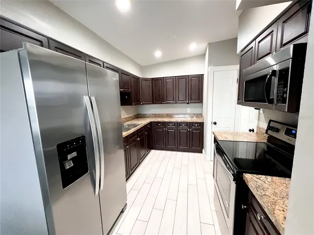 a kitchen with stainless steel appliances kitchen island granite countertop a refrigerator a sink a stove top oven and wooden floor