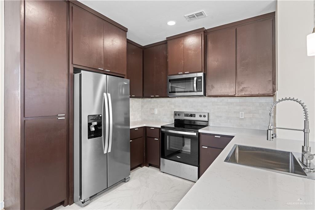 503 Sparrow Road Weslaco, TX 78596 - Photo 6 of 14 Contemporary kitchen featuring dark wood-finish cabinetry, stainless steel appliances, a subway tile backsplash, light-toned countertops, and a modern pull-down faucet