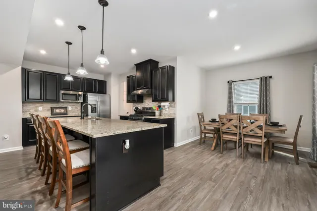 a kitchen with stainless steel appliances granite countertop a stove a refrigerator a kitchen island a dining table and chairs with wooden floor
