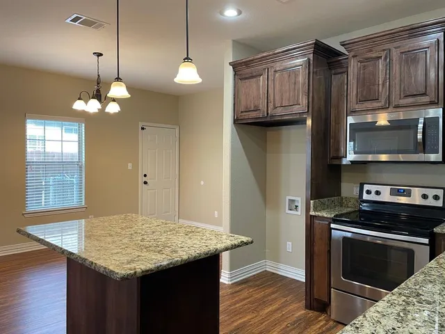 a kitchen with kitchen island granite countertop stainless steel appliances a stove cabinets and wooden floor