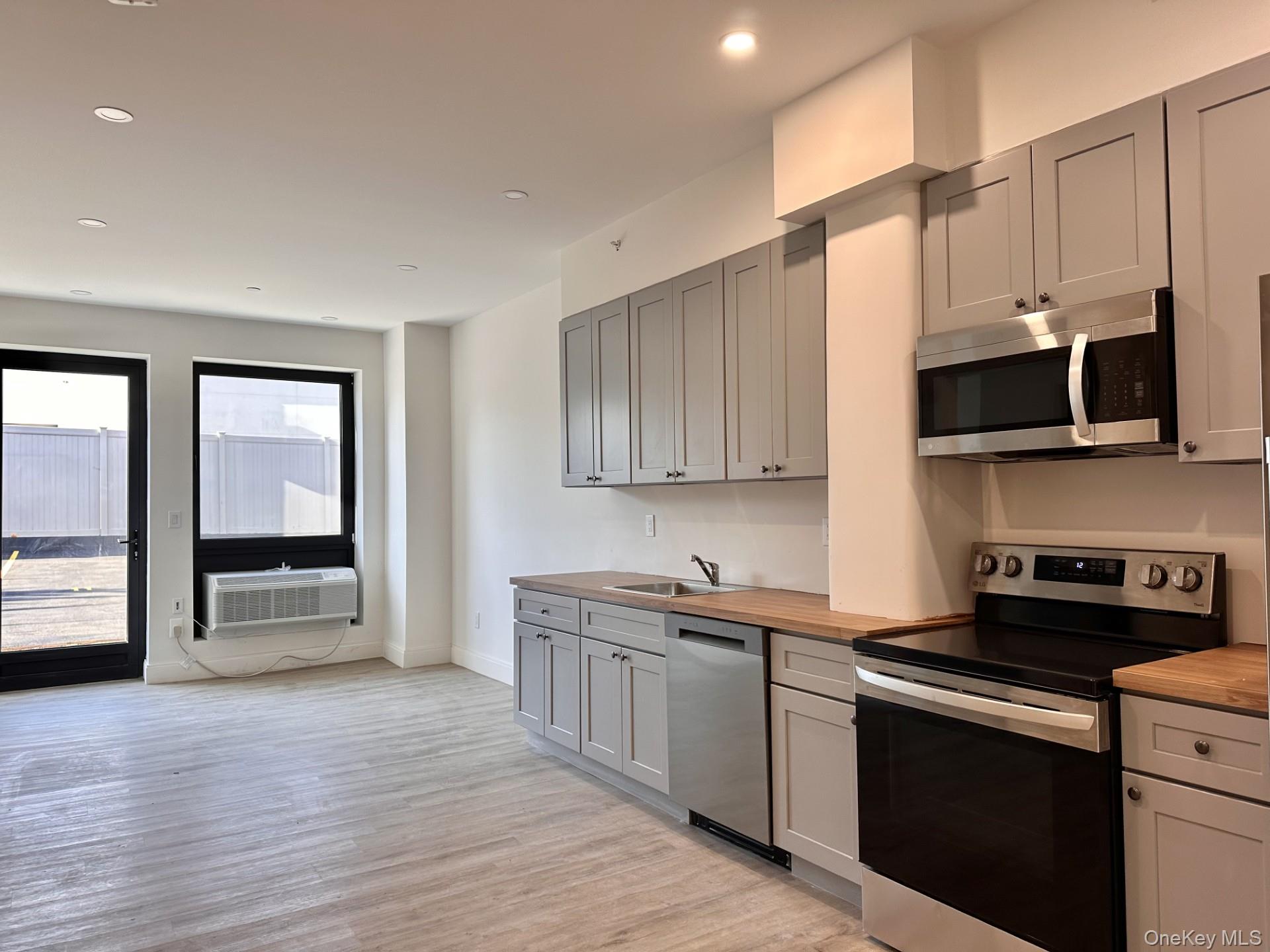 Kitchen with appliances with stainless steel finishes, gray cabinets, light wood-style floors, recessed lighting, and butcher block countertops