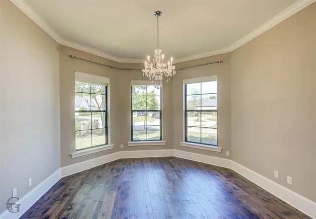 an empty room with wooden floor chandelier and windows