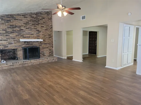 an empty room with wooden floor fireplace cabinet and windows