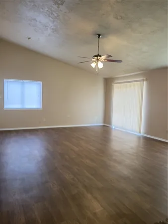 an empty room with wooden floor chandelier fan and windows