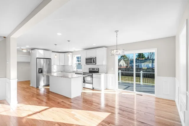 a open kitchen with stainless steel appliances granite countertop a refrigerator oven a sink dishwasher and white cabinets with wooden floor