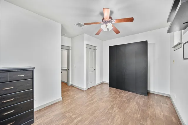 a view of an empty room with wooden floor and a ceiling fan