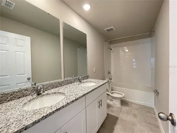 a bathroom with a granite countertop double vanity sink toilet mirror and bathtub