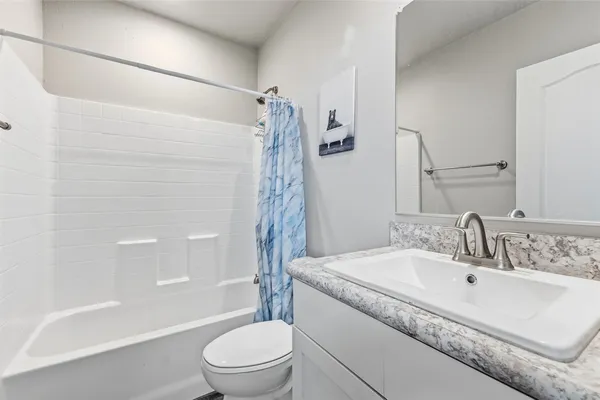 a bathroom with a granite countertop bathtub shower sink vanity and toilet