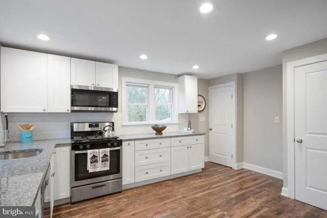 a kitchen with stainless steel appliances granite countertop wooden cabinets a sink a stove a dining table and chairs