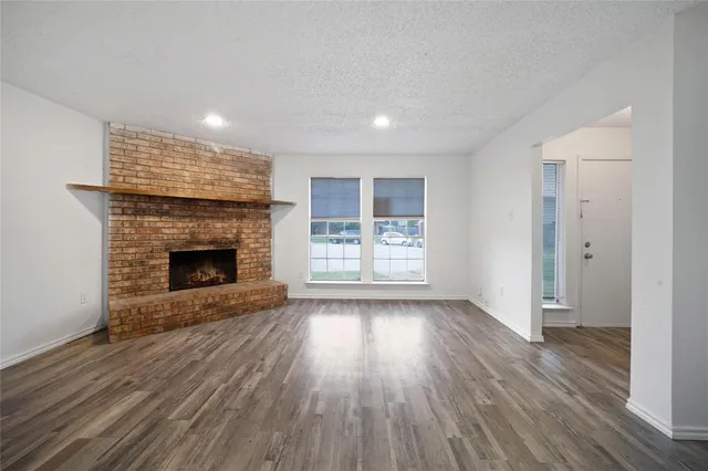 a view of an empty room with wooden floor fireplace and a window