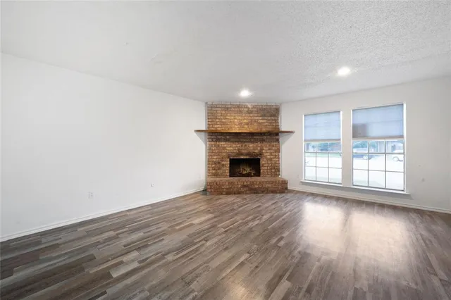 an empty room with wooden floor fireplace and windows