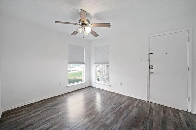 an empty room with wooden floor chandelier fan and windows