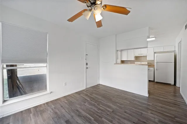 a view of empty room with wooden floor and kitchen view