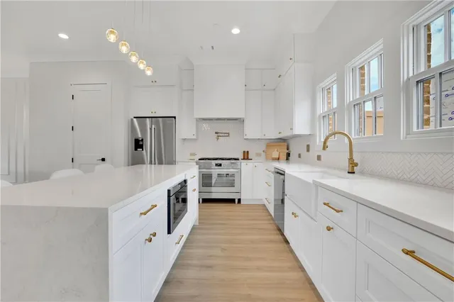 a large kitchen with stainless steel appliances sink a stove and white cabinets