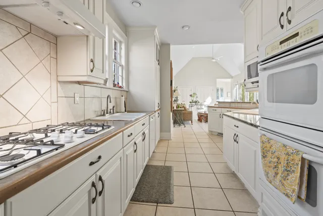 a large white kitchen with stainless steel appliances granite countertop a stove and a sink