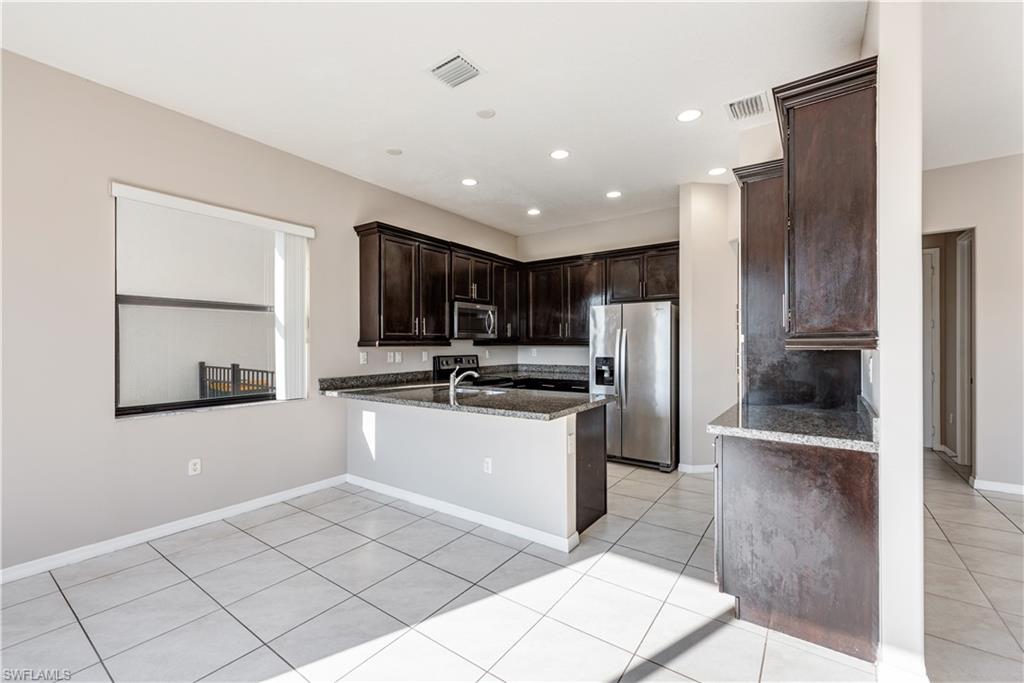 8732 Madrid Circle Naples, FL 34104 - Photo 5 of 15 Kitchen featuring dark stone counters, kitchen peninsula, appliances with stainless steel finishes, light tile patterned floors, and dark brown cabinetry