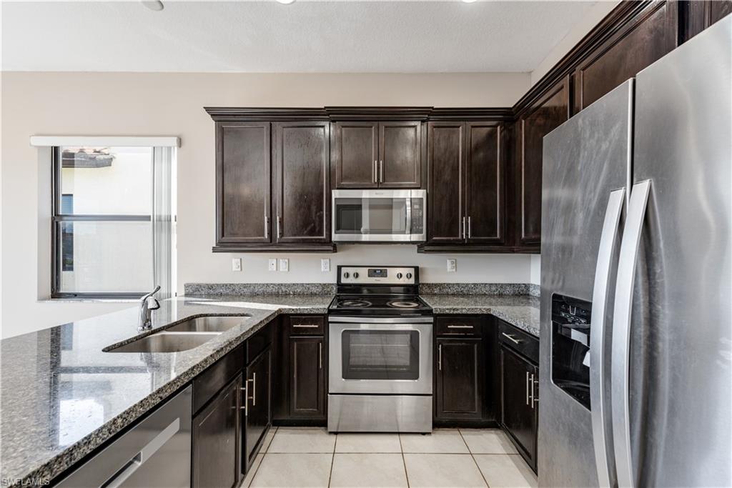 8732 Madrid Circle Naples, FL 34104 - Photo 6 of 15 Kitchen with light tile patterned flooring, stone countertops, stainless steel appliances, dark brown cabinetry, and sink
