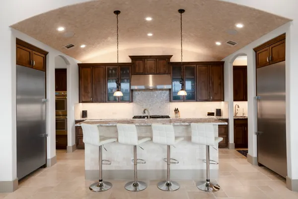 a kitchen with stainless steel appliances granite countertop a sink a stove a refrigerator cabinets and chairs