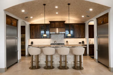 a kitchen with stainless steel appliances granite countertop a sink a stove a refrigerator cabinets and chairs