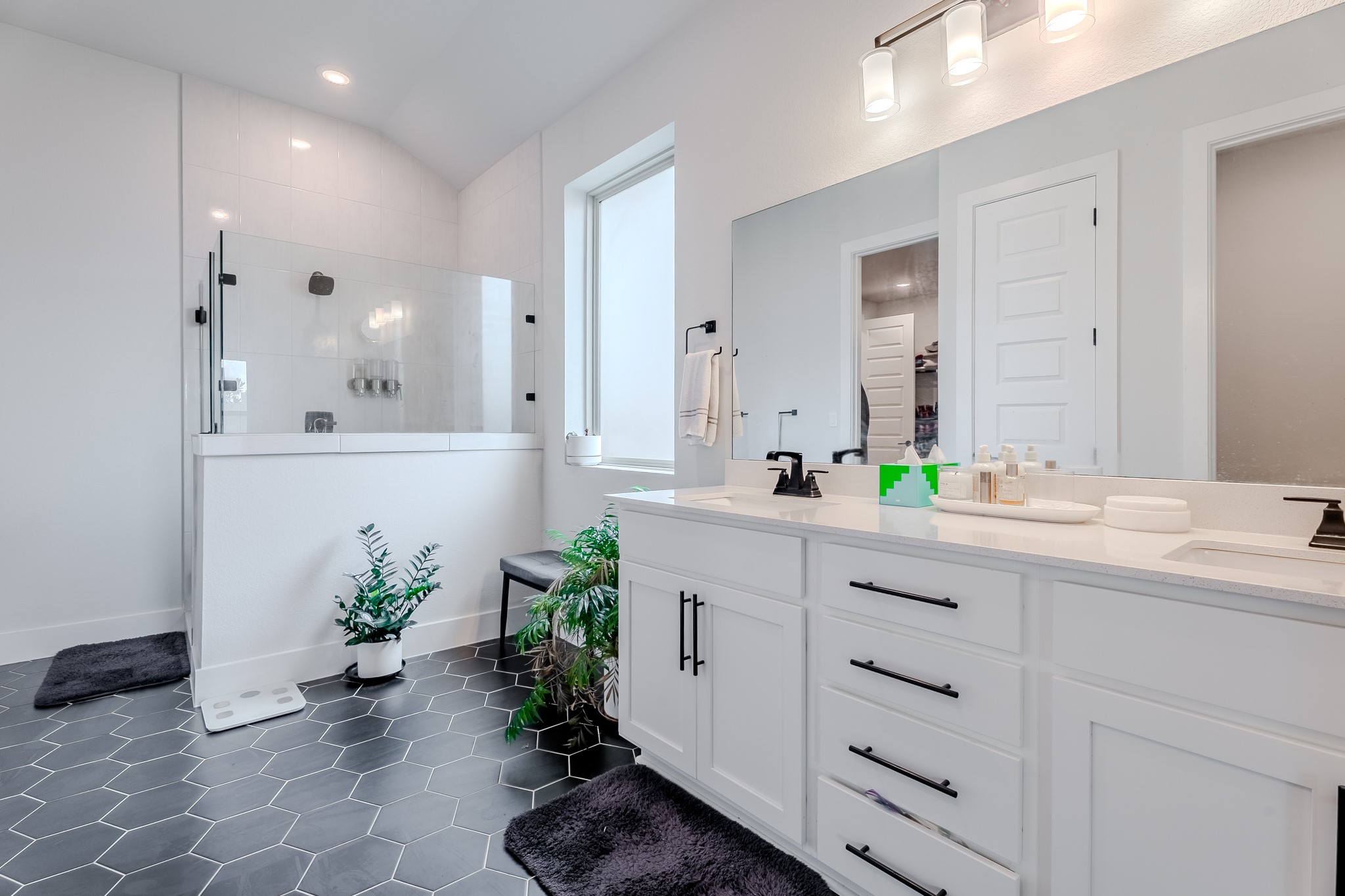 8109 Edmondson Bend Austin, TX 78744 - Photo 13 of 38 A contemporary primary bathroom featuring dual vanities, a glass-enclosed shower, and sleek hexagon tile flooring.