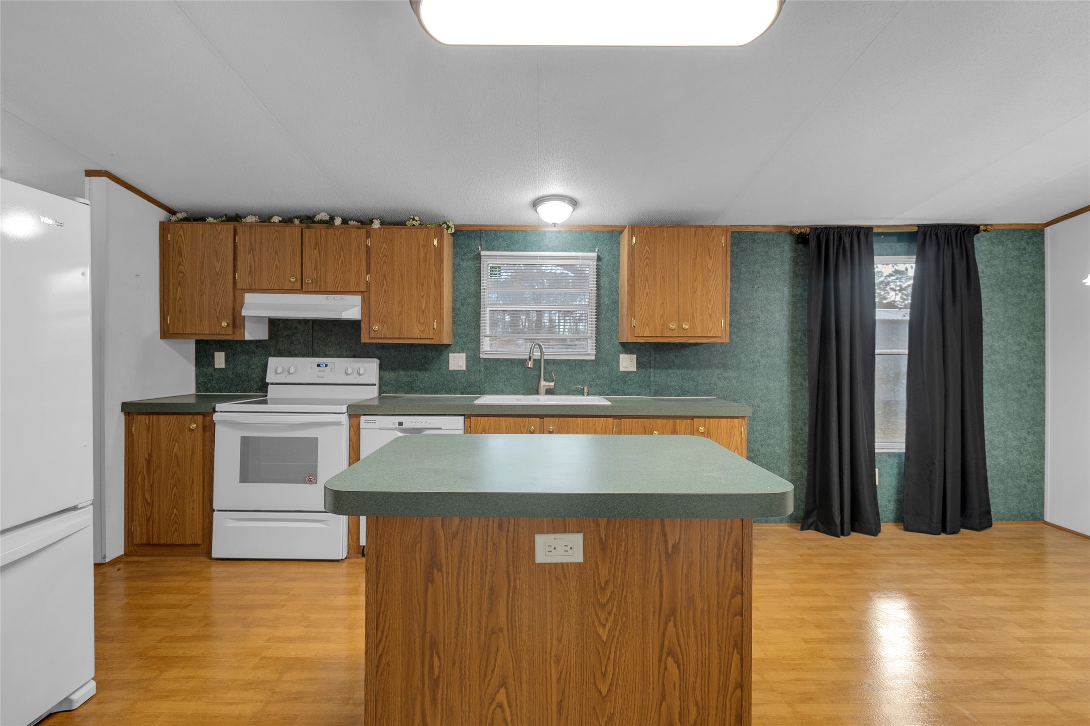 22094 Spear Road Porter, TX 77365 - Photo 8 of 45 This photo shows a cozy kitchen with wood cabinetry. It features an island, white appliances, and a window over the sink. The room is well-lit and has wood flooring, creating a warm and inviting atmosphere.