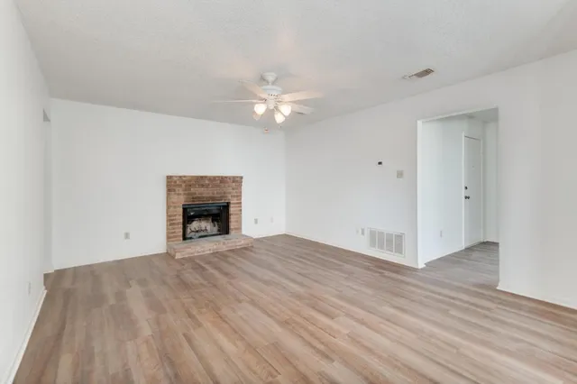 a view of an empty room with chandelier fan and fire place