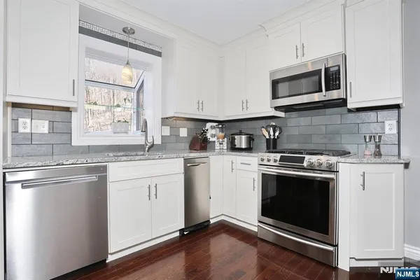 a kitchen with granite countertop white cabinets stainless steel appliances and a window