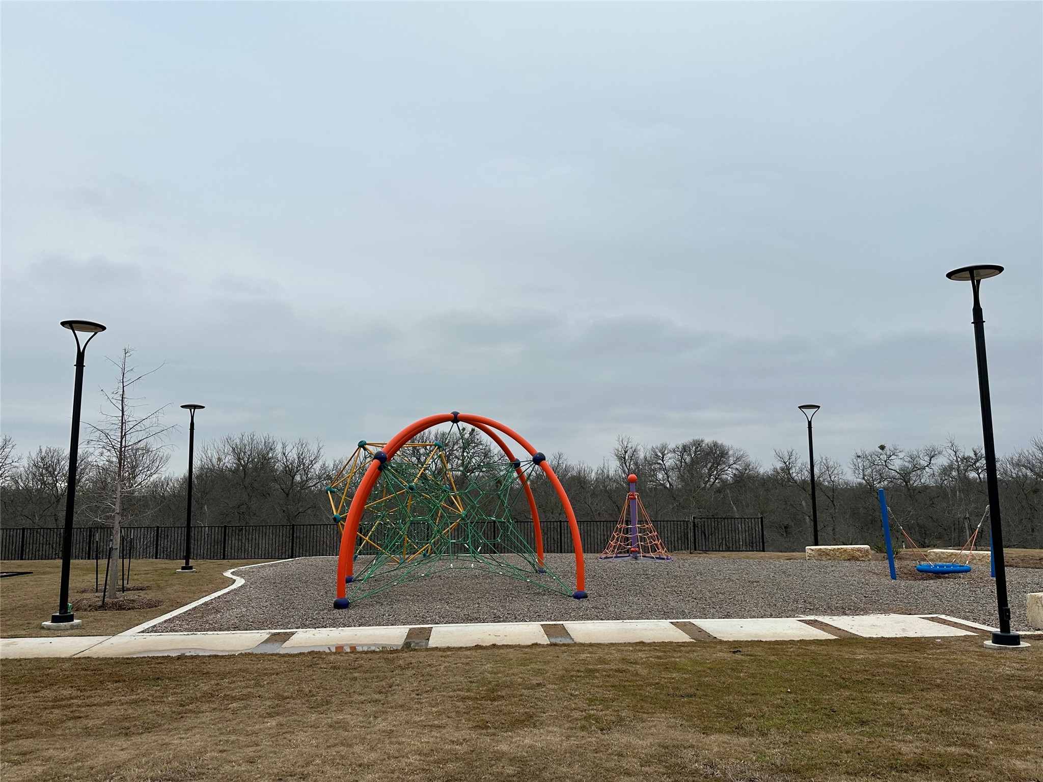 13501 Mussel Run Elgin, TX 78621 - Photo 20 of 28 Recreational area featuring modern play equipment, a gravel ground surface, mature trees bordering the perimeter, a concrete pathway, and contemporary street lighting fixtures